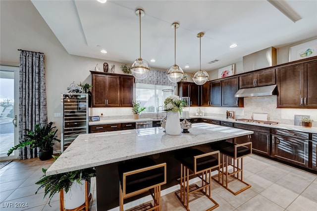 kitchen featuring a kitchen island, dark brown cabinetry, a kitchen bar, decorative light fixtures, and light stone counters