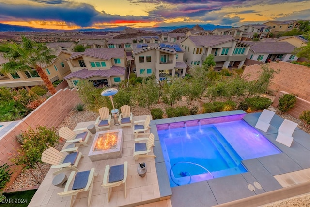 pool at dusk featuring a patio, a hot tub, pool water feature, and a fire pit