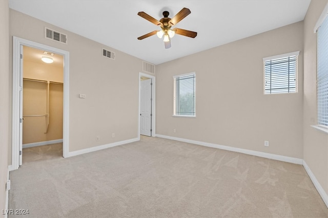 unfurnished bedroom with light carpet, a walk in closet, a closet, and ceiling fan