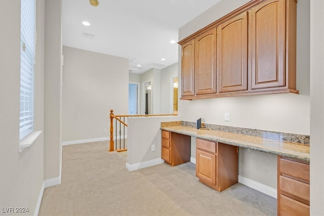 kitchen featuring built in desk, light stone countertops, and light carpet