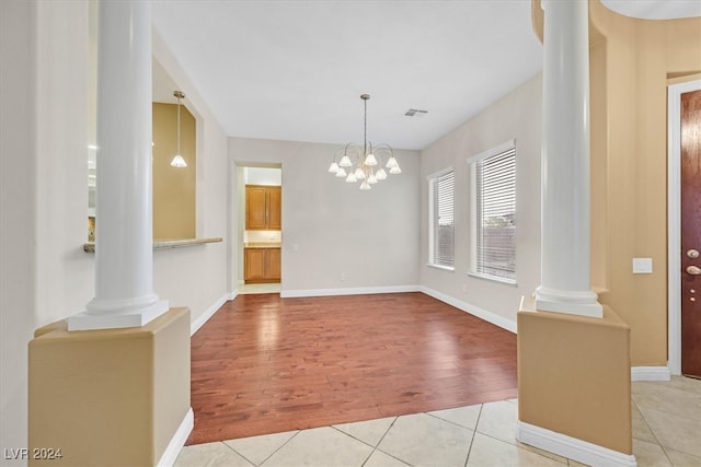 unfurnished dining area featuring ornate columns, a notable chandelier, and light hardwood / wood-style flooring