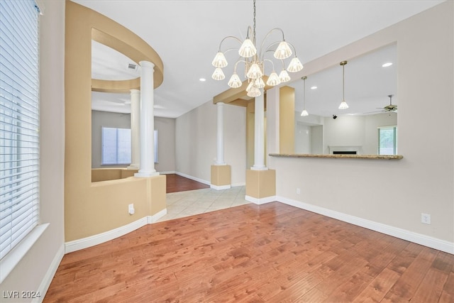 unfurnished dining area featuring ornate columns, light hardwood / wood-style floors, and ceiling fan with notable chandelier