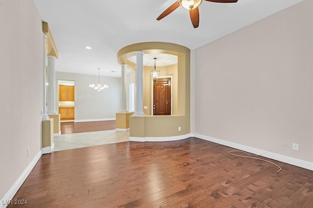 spare room featuring ornate columns, ceiling fan with notable chandelier, and light wood-type flooring