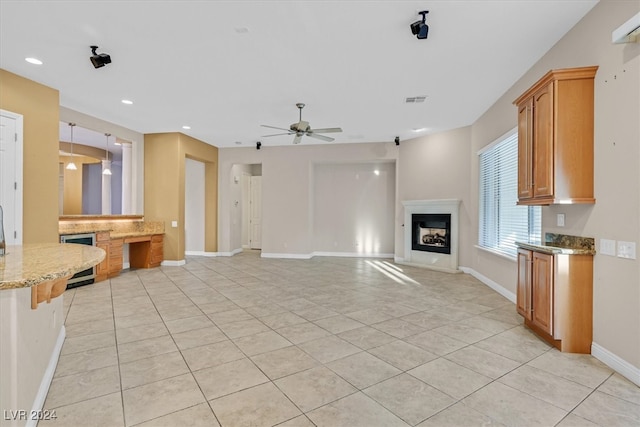 kitchen with ceiling fan, light tile patterned floors, light stone counters, and beverage cooler