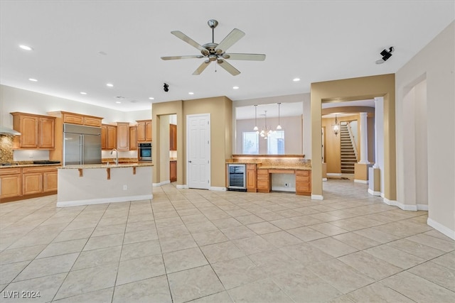 kitchen with stainless steel appliances, sink, a kitchen bar, beverage cooler, and ceiling fan with notable chandelier