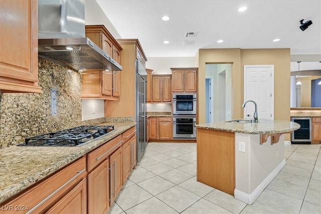 kitchen with wine cooler, light stone counters, stainless steel appliances, wall chimney exhaust hood, and sink