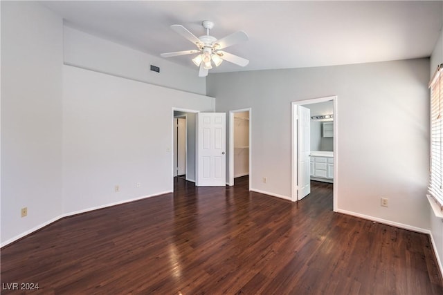 unfurnished bedroom featuring baseboards, visible vents, wood finished floors, a walk in closet, and vaulted ceiling