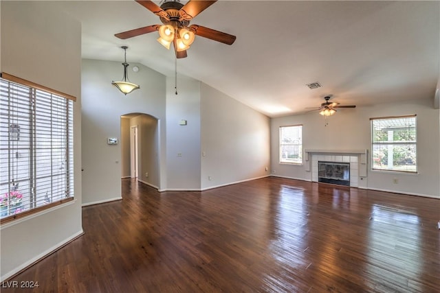 unfurnished living room featuring arched walkways, a fireplace, wood finished floors, and a healthy amount of sunlight