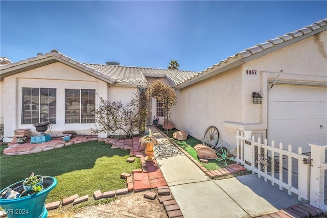 entrance to property featuring an attached garage, fence, a tiled roof, a lawn, and stucco siding