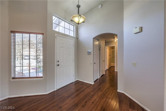 foyer with a healthy amount of sunlight, high vaulted ceiling, arched walkways, and dark wood finished floors