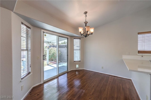 unfurnished dining area with dark wood-style floors, a notable chandelier, and baseboards