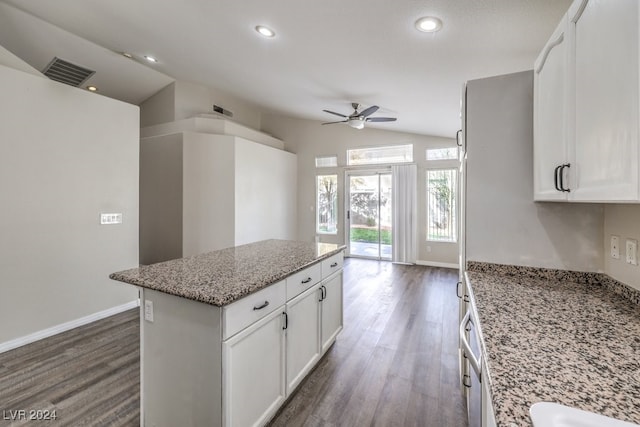 kitchen with light stone countertops, a center island, white cabinets, and vaulted ceiling