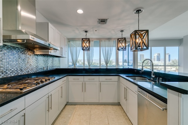 kitchen with wall chimney range hood, sink, white cabinetry, stainless steel appliances, and pendant lighting