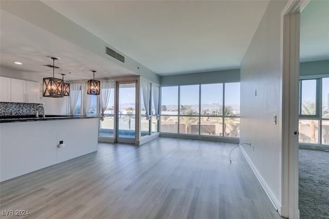 unfurnished living room featuring sink, light hardwood / wood-style flooring, and a notable chandelier