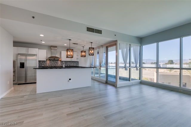 kitchen featuring wall chimney range hood, hanging light fixtures, light wood-type flooring, white cabinetry, and stainless steel built in refrigerator