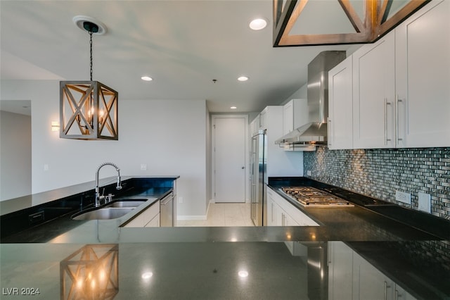 kitchen featuring wall chimney exhaust hood, hanging light fixtures, stainless steel appliances, sink, and white cabinets