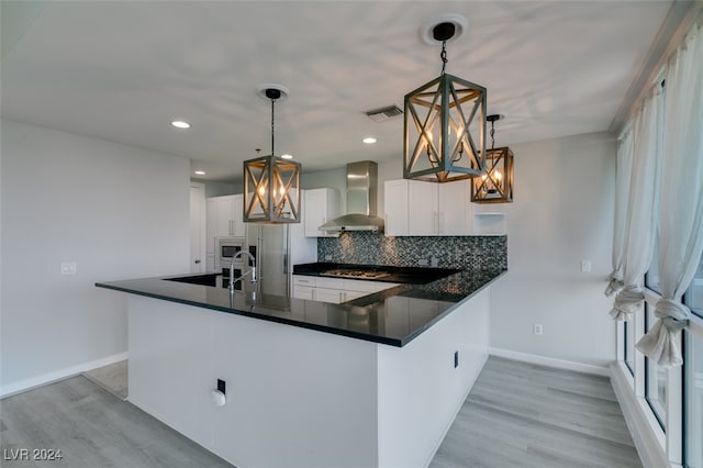 kitchen featuring white cabinetry, wall chimney range hood, decorative light fixtures, and kitchen peninsula