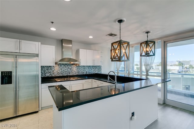 kitchen with decorative backsplash, wall chimney exhaust hood, hanging light fixtures, white cabinetry, and appliances with stainless steel finishes