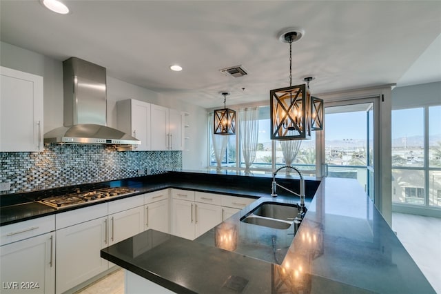 kitchen with pendant lighting, white cabinets, wall chimney range hood, and stainless steel gas cooktop