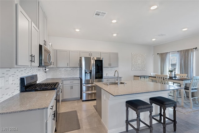 kitchen with tasteful backsplash, light stone counters, an island with sink, appliances with stainless steel finishes, and sink