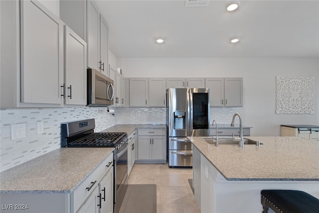 kitchen with sink, backsplash, a kitchen breakfast bar, stainless steel appliances, and light stone counters