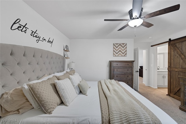 carpeted bedroom with a barn door, ensuite bathroom, and ceiling fan