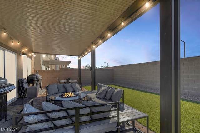 patio terrace at dusk featuring an outdoor living space with a fire pit, grilling area, and a lawn