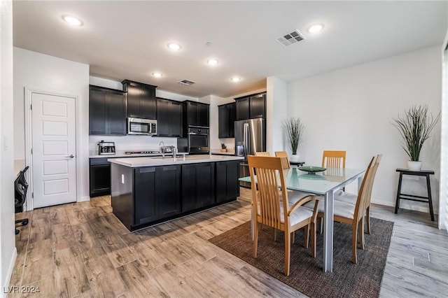 kitchen with appliances with stainless steel finishes, light hardwood / wood-style floors, a center island with sink, and sink