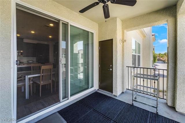 view of exterior entry with ceiling fan and a balcony