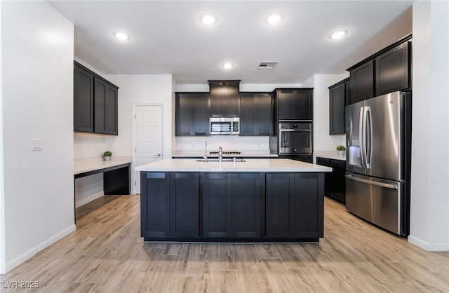 kitchen with appliances with stainless steel finishes, sink, light hardwood / wood-style flooring, and a kitchen island with sink