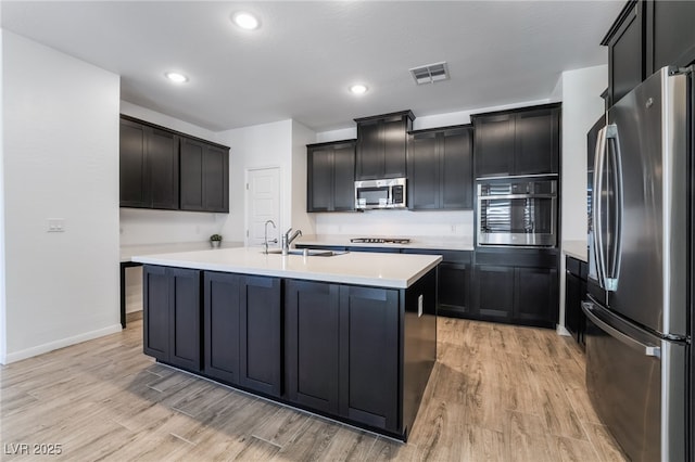 kitchen with light hardwood / wood-style floors, sink, appliances with stainless steel finishes, and a kitchen island with sink