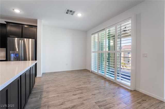 kitchen with light stone counters, light hardwood / wood-style floors, and stainless steel fridge with ice dispenser