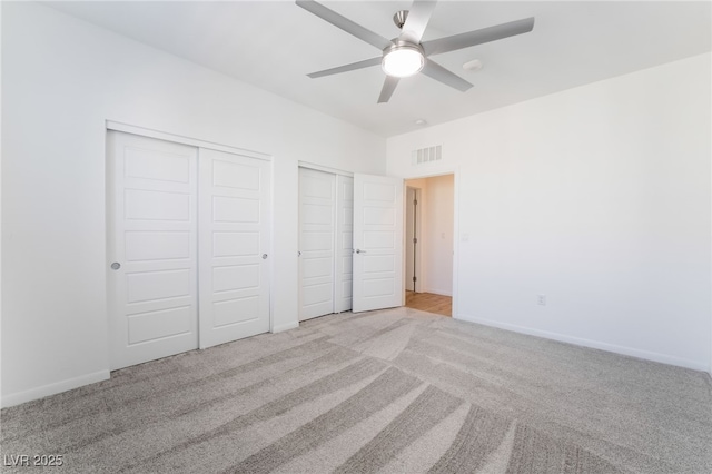 unfurnished bedroom with ceiling fan, light colored carpet, and two closets