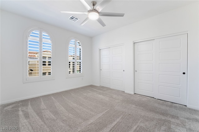 unfurnished bedroom with ceiling fan, light colored carpet, and multiple closets