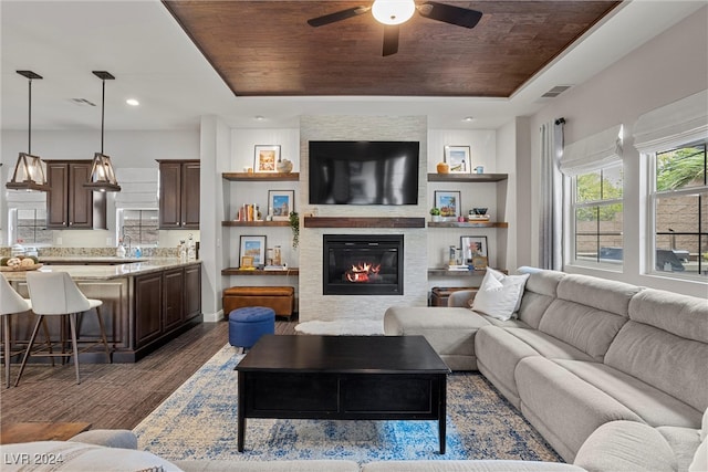 living room with dark wood-type flooring, wood ceiling, a tray ceiling, and ceiling fan