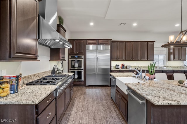 kitchen with wall chimney range hood, appliances with stainless steel finishes, dark hardwood / wood-style floors, pendant lighting, and sink