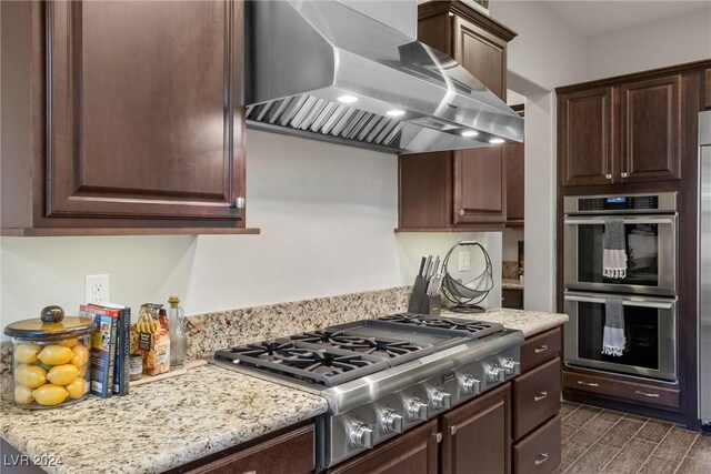 kitchen featuring dark wood-type flooring, light stone countertops, wall chimney exhaust hood, and appliances with stainless steel finishes