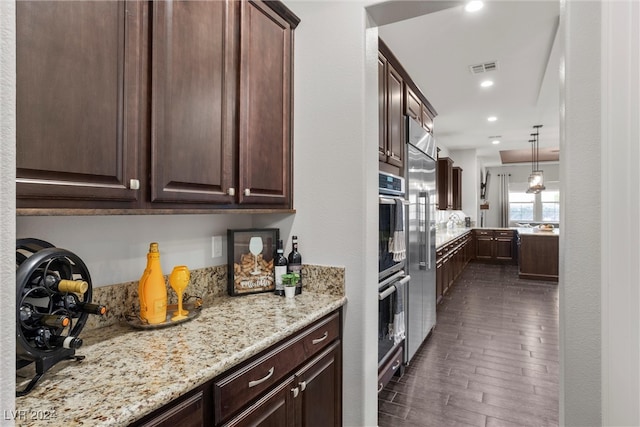 kitchen with light stone countertops, dark brown cabinets, dark hardwood / wood-style flooring, double oven, and decorative light fixtures