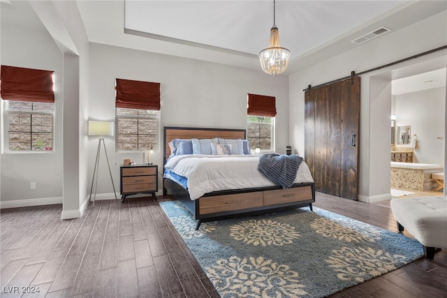 bedroom featuring ensuite bath, an inviting chandelier, dark hardwood / wood-style flooring, and a barn door