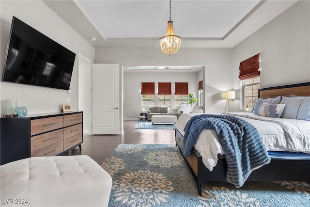 bedroom with dark wood-type flooring, a tray ceiling, and a chandelier