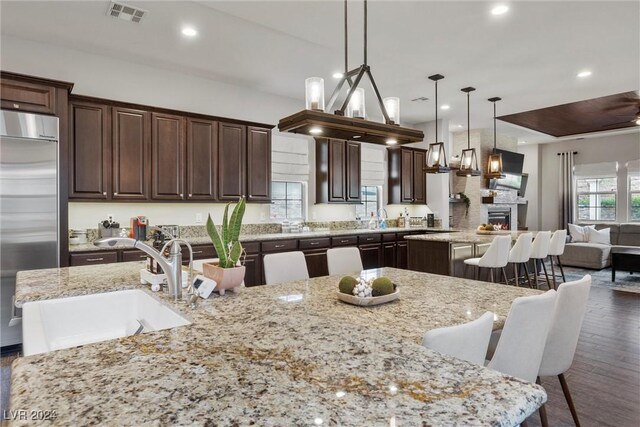 kitchen featuring stainless steel built in refrigerator, a breakfast bar area, a large island with sink, dark wood-type flooring, and decorative light fixtures