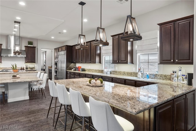 kitchen with dark wood-type flooring, wall chimney range hood, pendant lighting, and a kitchen island