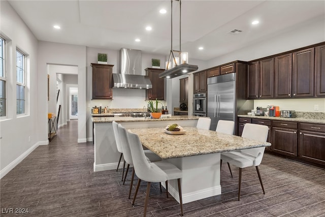 kitchen featuring wall chimney exhaust hood, a kitchen breakfast bar, a center island, and hanging light fixtures