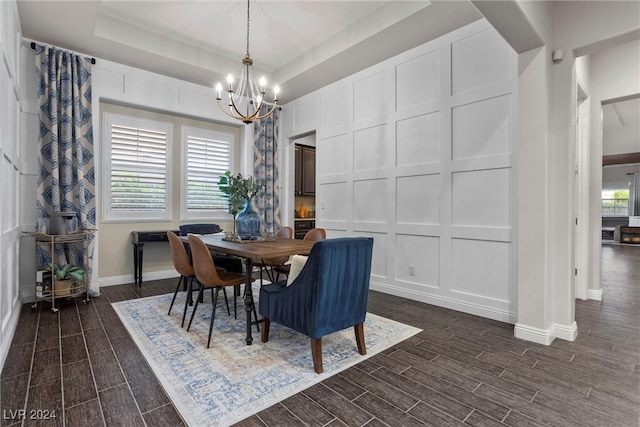 dining room featuring a notable chandelier, dark wood-type flooring, and a raised ceiling