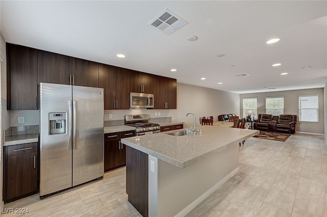 kitchen with appliances with stainless steel finishes, a kitchen island with sink, sink, and dark brown cabinets