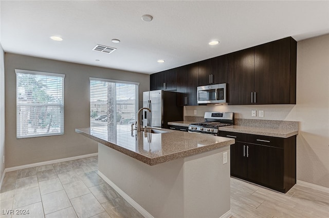 kitchen featuring stainless steel appliances, dark brown cabinets, sink, and a kitchen island with sink