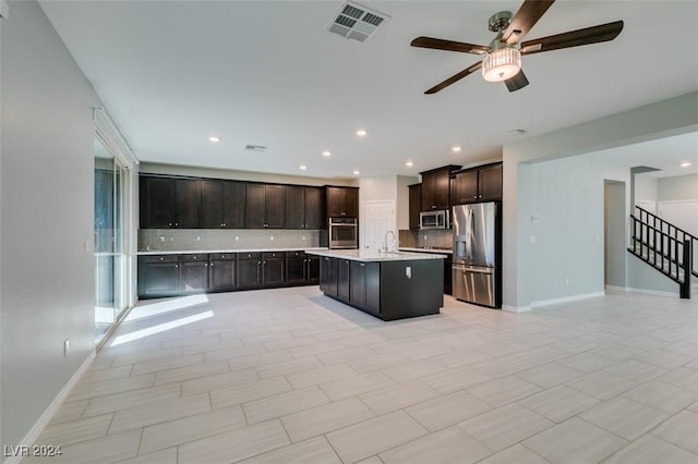 kitchen featuring decorative backsplash, dark brown cabinetry, stainless steel appliances, and an island with sink