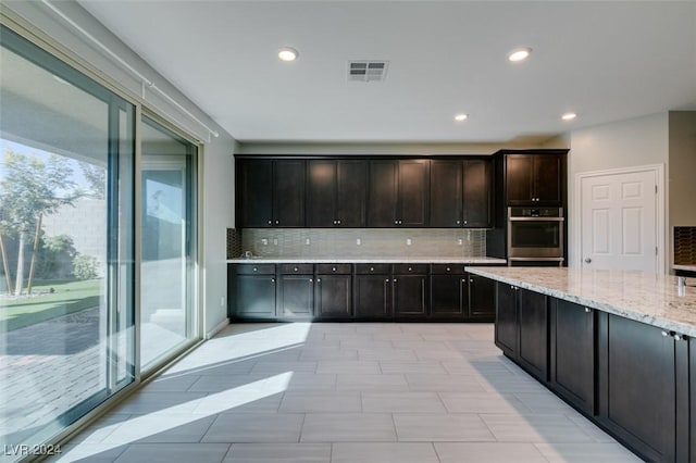 kitchen featuring light stone counters, backsplash, double oven, and dark brown cabinets