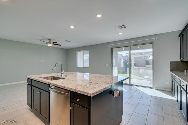 kitchen with light stone countertops, dishwasher, sink, ceiling fan, and a center island with sink