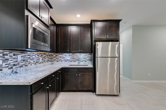 kitchen featuring appliances with stainless steel finishes, decorative backsplash, light stone counters, dark brown cabinetry, and sink